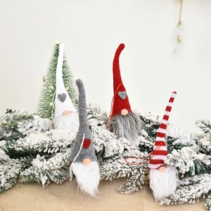 Set of four Nordic Christmas gnome ornaments with felt hats on snowy pine branches