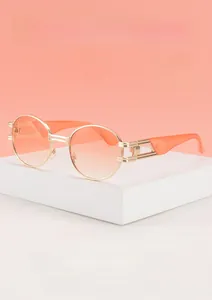 Détail de lunettes de soleil ovales en métal doré avec verres dégradés orange et découpes