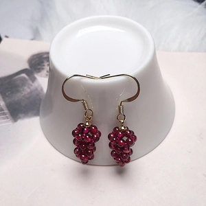 Detailed view of handmade pomegranate red garnet grape earrings hanging on a ceramic cup