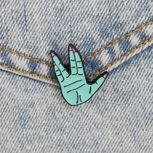Detail of a mint green Vulcan hand gesture enamel pin on blue denim fabric background