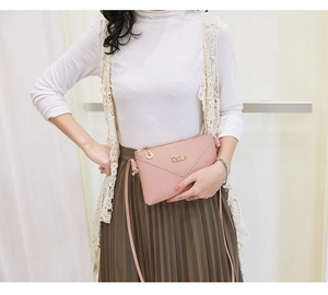 Detailed shot of a pink envelope crossbody bag with a gold leaf pendant and logo