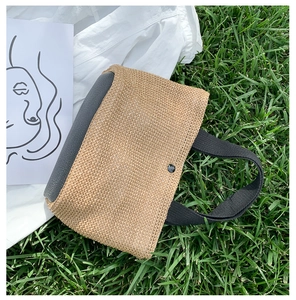 Detail view of woven straw tote bag with black leather handles on lush green grass