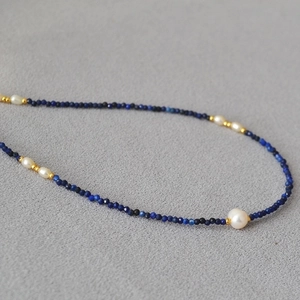 Lapis lazuli beaded necklace with freshwater pearls and gold accents on gray fabric