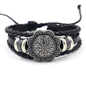 Dettaglio del bracciale in pelle intrecciata con stemma metallico e motivo floreale vintage