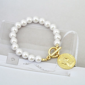 Detailed macro of baroque pearl bracelet with gold OT clasp and embossed coin pendant