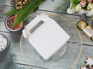 White gift box with handle among festive Christmas decorations and snacks on a table