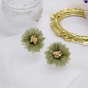 Boucles d'oreilles fleurs en mousseline vert Morandi avec pistil blanc sur tissu blanc