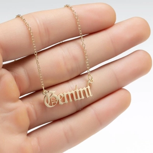 Close-up of golden Gemini zodiac necklace pendant held by hand on grey background