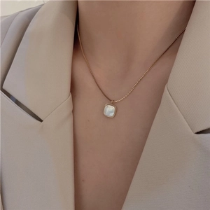 Detail of a gold square necklace with white mother of pearl inlay on a model in a beige suit