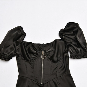 Detail of black satin top featuring puff sleeves, front zipper, and V-shaped hemline