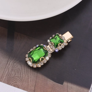 Detail of a gold metal hair clip with green gemstones and sparkling rhinestones