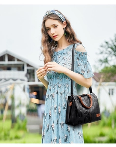 Detail of black leather handbag with embossed letters and brown handles carried outdoors