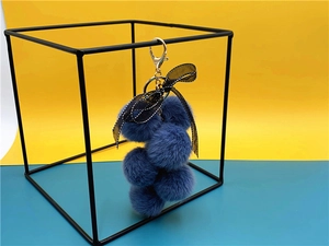 Blue plush grape keychain with a black bow hanging on a modern metal frame display