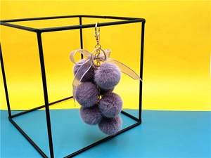 Detail of purple grape-shaped plush keychain with lace bow and gold metal spring clasp