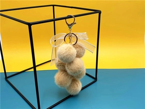 Detail of plush grape keychain with beige fur balls, organza bow and metal lobster clasp