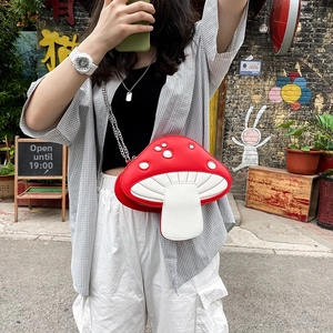 Street style shot of a cute red mushroom cross-body bag with silver metal chain strap