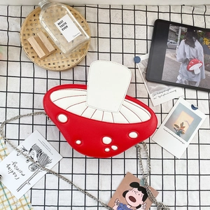 Top view of red and white mushroom-shaped crossbody bag with silver chain on checkered cloth