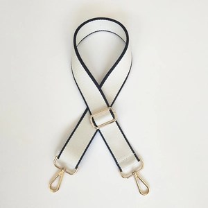 Close-up of cream canvas bag strap with black piping and gold adjustable buckles
