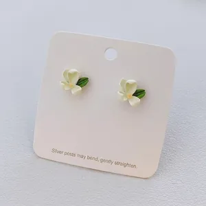 Macro detail of tulip flower stud earrings with white petals and green leaf on cards