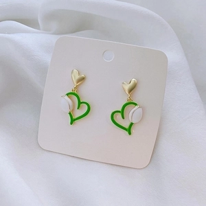 Detail of floral heart drop earrings with green enamel outline and gold finish charms