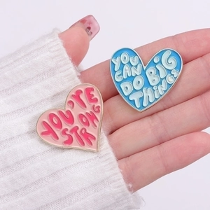 Inspirational heart enamel pins in pink and blue on white sweater background