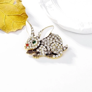 Sparkling crystal rabbit brooch with green eyes and red nose on elegant gold leaf background