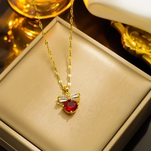 Elegant gold titanium steel necklace with a red gemstone bow pendant on a jewelry box