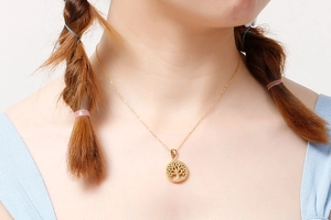 Detailed view of a gold hollow tree of life pendant necklace worn by a fashion model