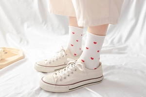 Detailed view of white mid-calf socks with red heart patterns and ruffled edges on model