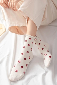 Close-up of cream crew socks with red floral pattern on soft white bedding