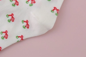 Close-up of white cotton crew socks with detailed red and green cherry patterns