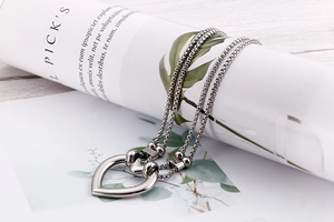 Detailed view of silver double-layered stainless steel heart necklace on magazine
