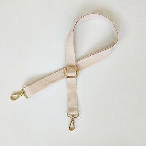 Detail of beige canvas bag strap with adjustable gold lobster clasps on white background