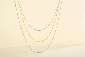 Detailed view of layered gold and silver stainless steel cable chains on beige background