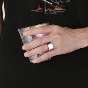 Close-up of a wide square stainless steel ring with hammered texture worn by a model