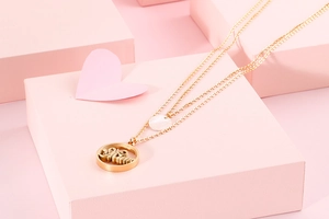 Detail view of a gold double-layer necklace with Mom pendant on a pink display stand