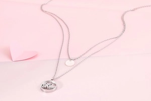 Detailed macro view of silver layered Mom pendant necklace on pink heart background