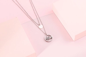 Detail of silver double-layer necklace with circular 'Mum' pendant on pink background