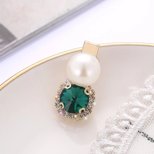 Elegant gold hair clip with large white pearl and green gemstone surrounded by rhinestones