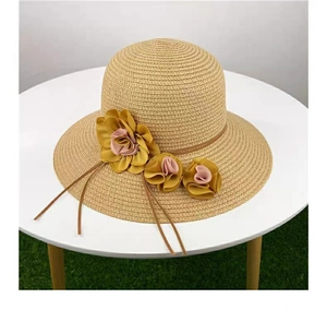 Detail of khaki straw sun hat with pink floral decoration on a white table