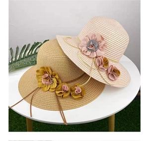 Detail of woven straw sun hats featuring large fabric flowers in khaki and pink colors