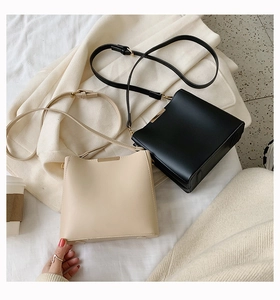 Detail of square PU leather crossbody bucket bags in black and beige with metal buckles