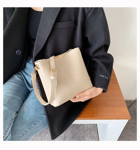 Detail of a creamy white bucket bag with gold metal hardware held by a model in a suit