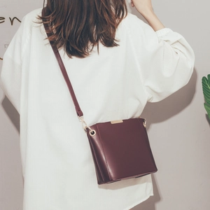 Elegant deep red leather bucket bag with gold hardware worn by a model in a white shirt
