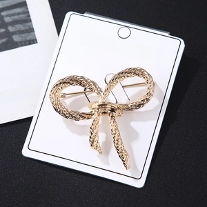 Detailed close-up of golden bow brooch with twisted rope texture on fashion card