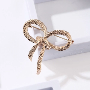 Detail of golden bow brooch with twisted rope texture on a white display stand