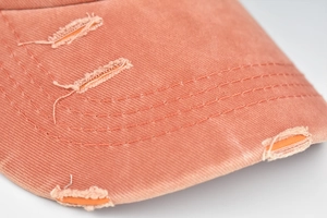Détail de la visière vieillie et des coutures sur une casquette queue de cheval rose