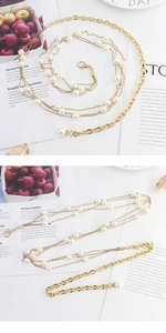 Detailed close-up of multi-layer gold metal waist chain with white faux pearl accents