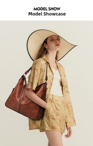 Brown leather tote bag worn by model featuring vertical stitching and top handles