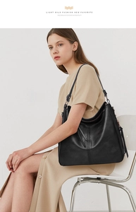Fashionable black leather hobo tote bag with fringe detail worn by a model in beige dress